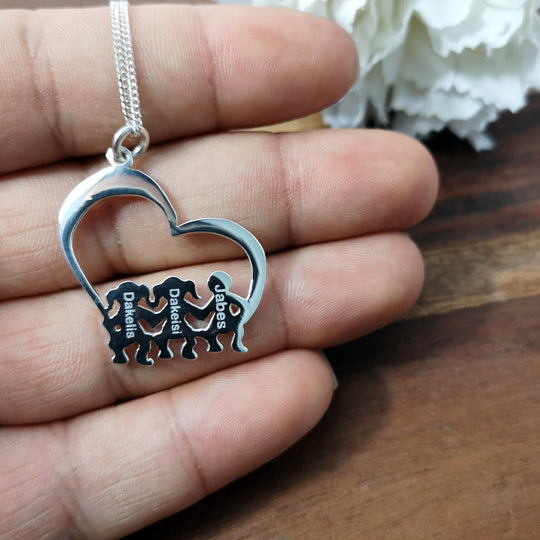 Detalle cercano del dije en forma de corazón con niños sentados, mostrando el grabado personalizado.