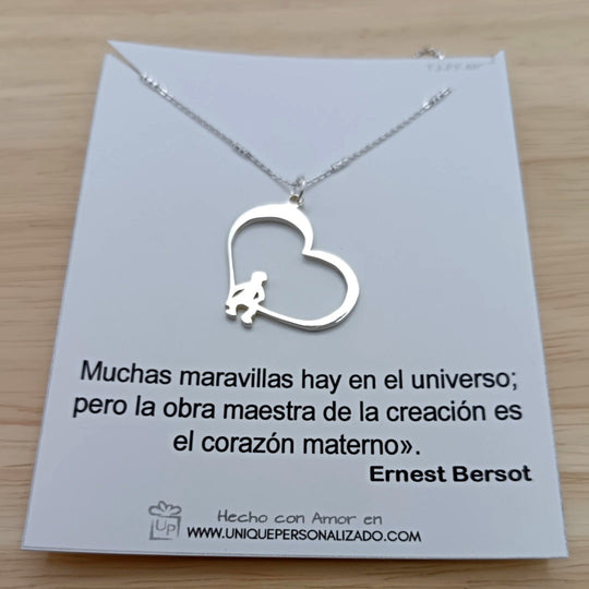 Vista frontal de la cadena con dije de corazón y figuras de niños sentados, en acabado brillante.