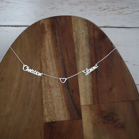 Primer plano del dije con los dos nombres y el corazón en el centro, mostrando detalles del corte y grabado.